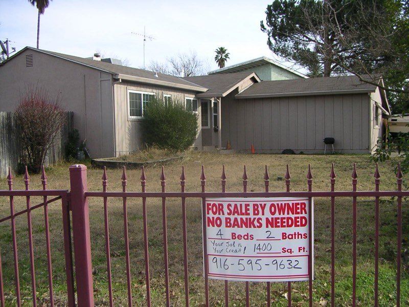 Bank-owned for-sale sign in front of a foreclosed house